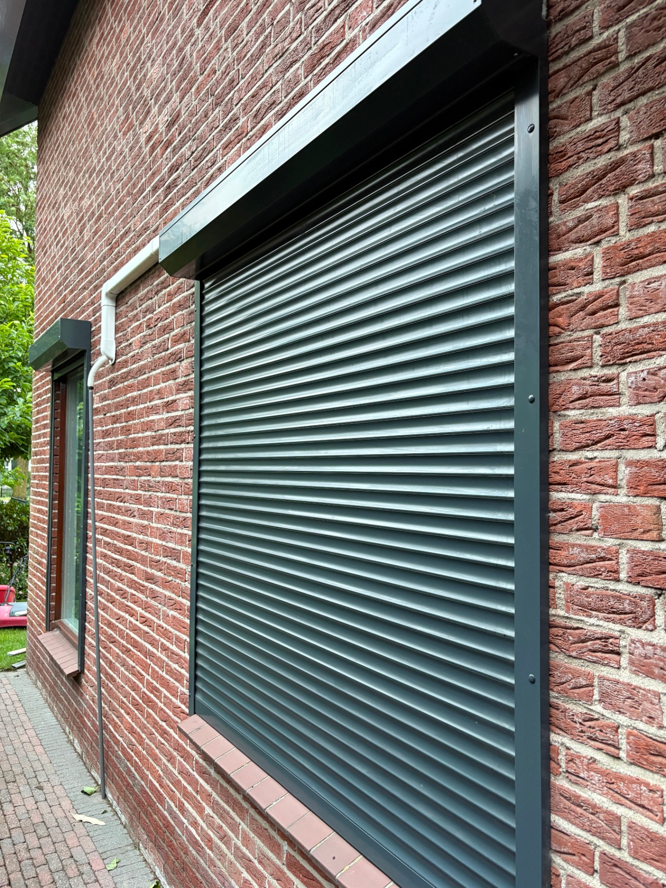 Twee antraciet rolluiken strak geplaatst op een bakstenen gevel